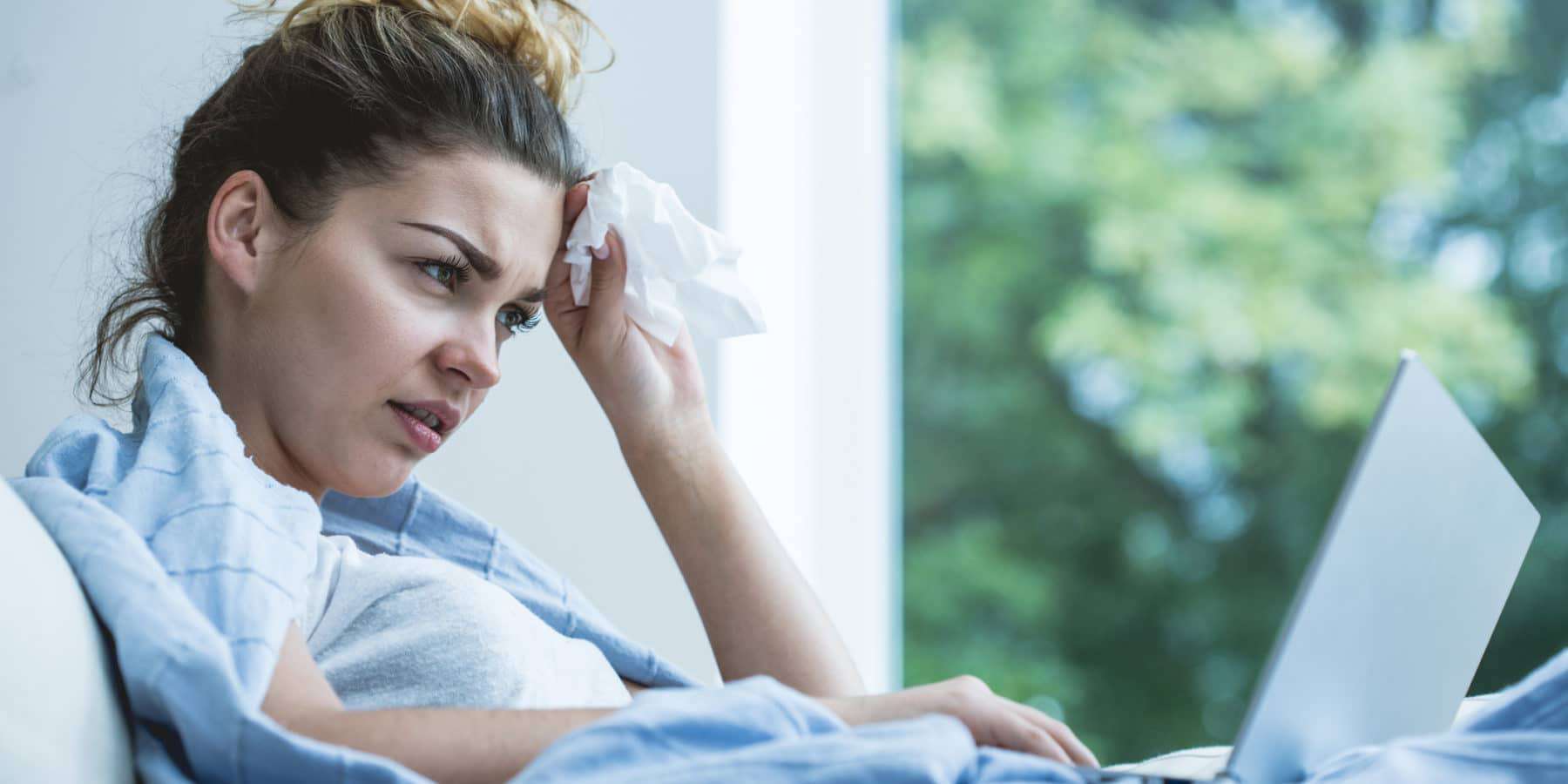 Sick woman sitting in bed looking up symptoms of black mold poisoning online.