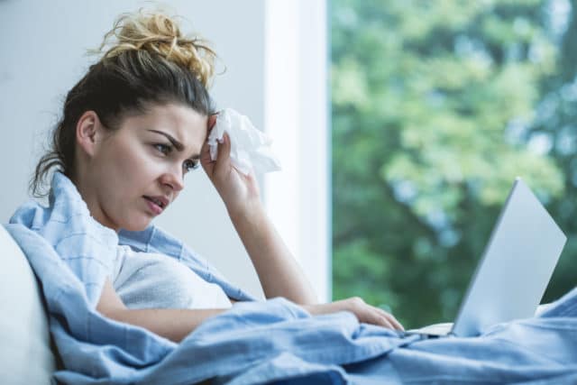 Sick woman sitting in bed looking up symptoms of black mold poisoning online.