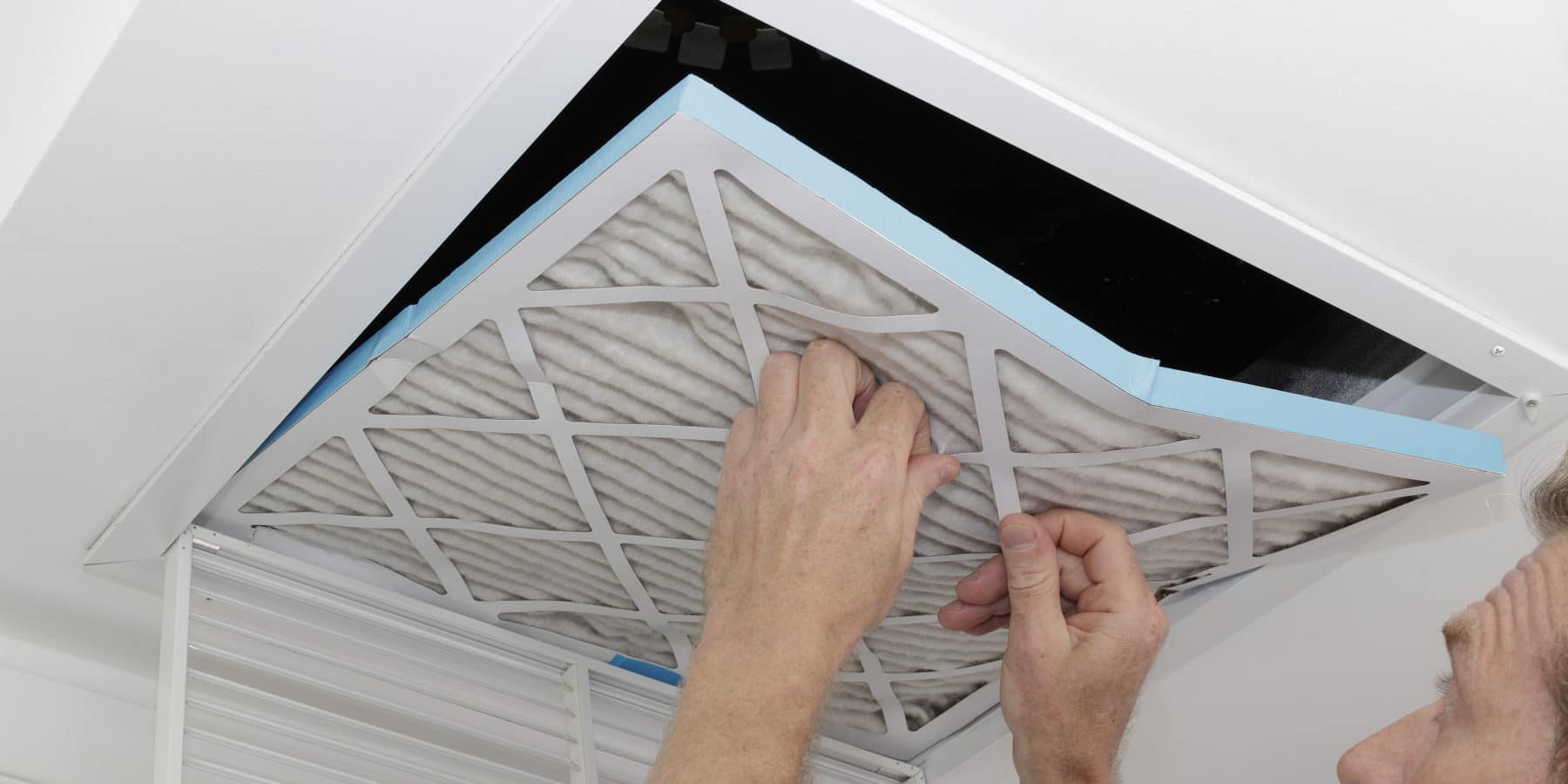 Person removing an old dirty air filter from a ceiling intake vent of a home HVAC system to improve indoor air quality.