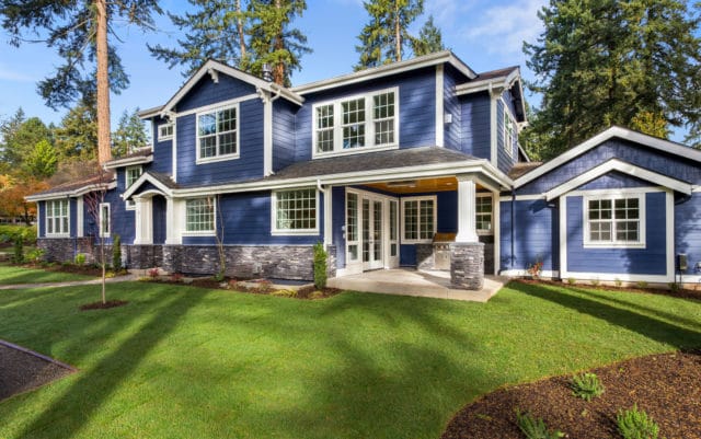 facade of home with manicured lawn, and backdrop of trees and blue sky